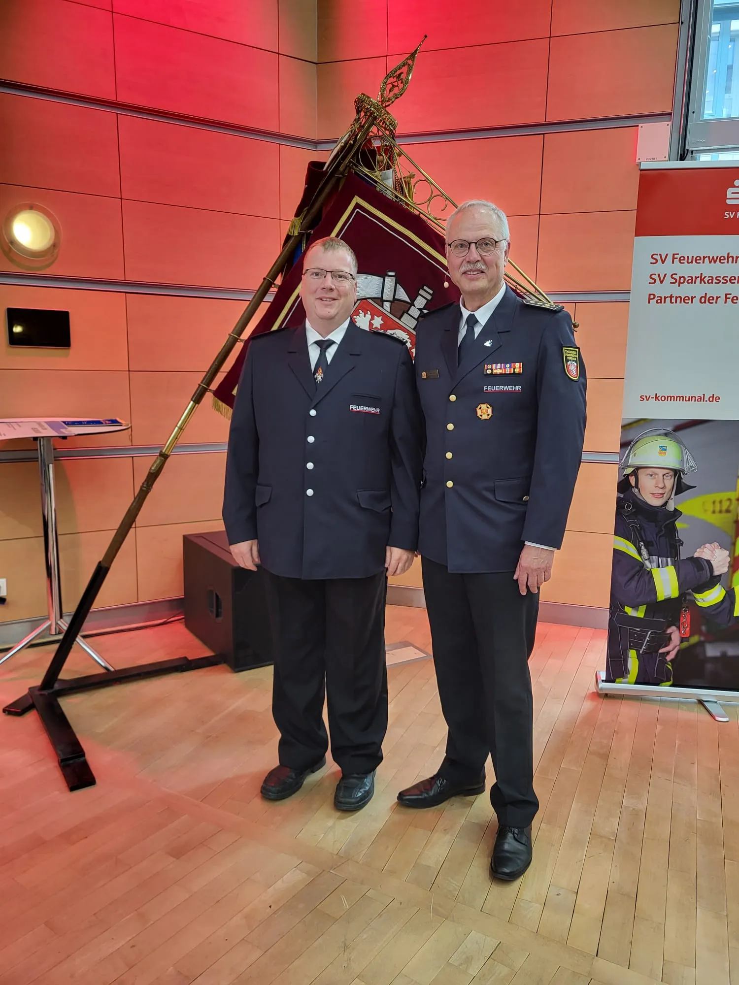 Kreisfeuerwehrverband Schmalkalden-Meiningen e.V. - Koordiniert die Aktivitäten und Veranstaltungen der Feuerwehr - Zwei junge Leute in dunkelblauen Feuerwehruniformen mit gelben Reflexstreifen bedienen einen Wasserschlauch während einer Übung im Freien.